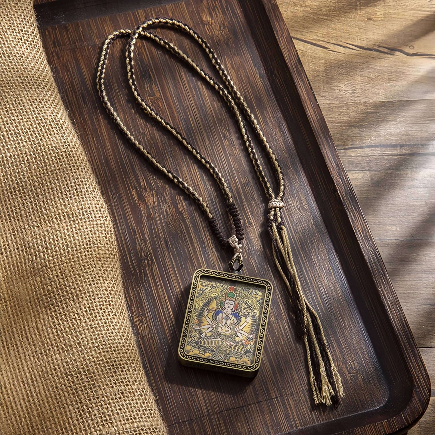 Tibetan Thangka Eight Protector Deities Pendant on a wooden tray with braided cord and tassel.