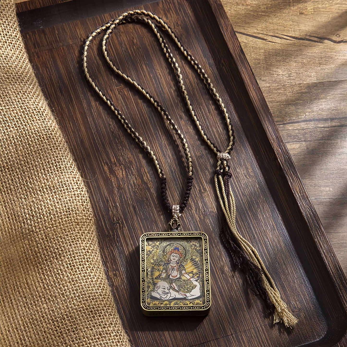 Tibetan Thangka Eight Protector Deities Pendant with intricate painting and braided cord on wooden tray.